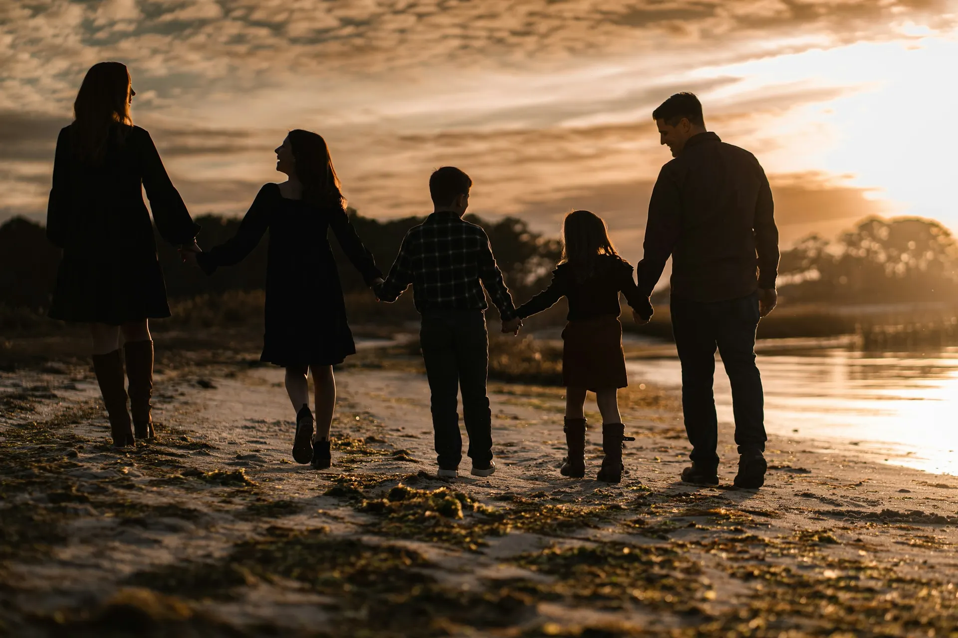 Eine Familie geht bei Sonnenuntergang Hand in Hand am Strand entlang